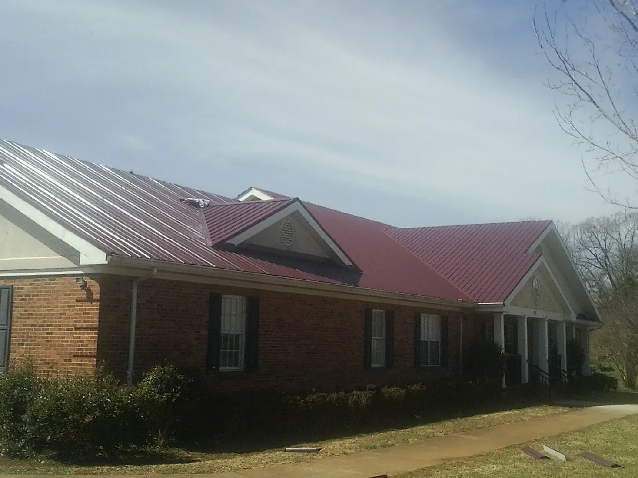 Red metal roof with gabled entries on a long brick building, from a Hail Damage Roof Repair job in Florence